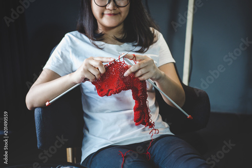 Close up shot of young woman hands knitting a red scarf handicraft in the living room on terrace at home