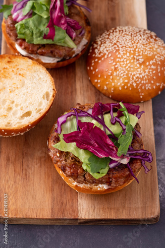 Beef burgers with vegetables. Flat lay on black textured background with sesame seeds. Top view.