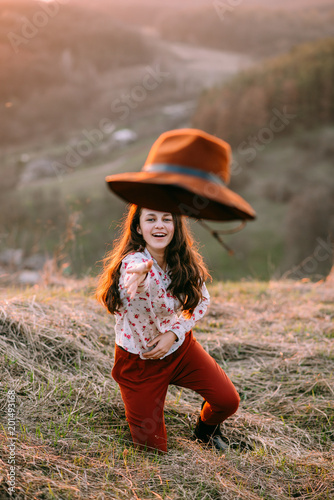 Portrait of a attractive young girl with a hat in the mountains at sunset. She resting and sitting wearing stylish fall outfit. Concept travel