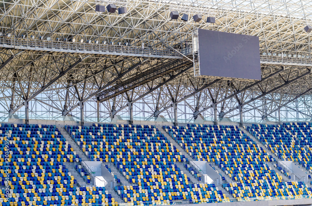 Naklejka premium Siedzący kibice kolorowe plastikowe krzesła na tle stadionu piłkarskiego. Pusty stadion boisko do piłki nożnej zielona trawa na arenie lekkoatletycznej piłki nożnej.