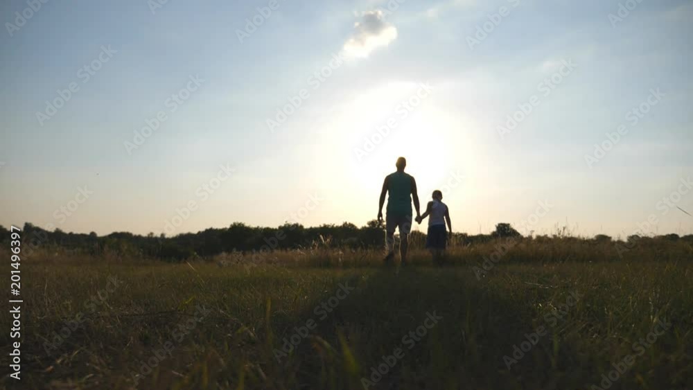 Silhouette of father and son walking on the field at sunset and holding hands of each other. Happy family spending time together outdoor. Active lifestyle. Slow motion Rear back view Silhouette of father and son walking on the field at sunset and holding hands of each other. Happy family spending time together outdoor. Active lifestyle. Slow motion Rear back view