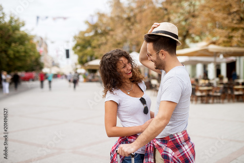 Young adorable couple is laughing on the street while standing on the city square facing each other and laughing.