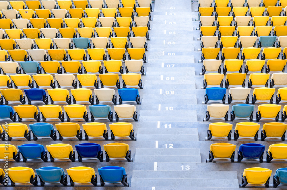 Fototapeta premium Siedzący kibice kolorowe plastikowe krzesła na tle stadionu piłkarskiego. Pusty stadion boisko do piłki nożnej zielona trawa na arenie lekkoatletycznej piłki nożnej.