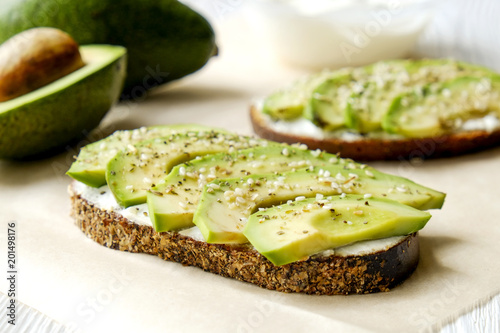 Vegan sandwich, rye bread toast, avocado slices, vegenaise sauce & raw arugula. Toasted sourdough, eggless mayonnaise, wooden table, whole & halved. National avocado day concept. Close up, background.