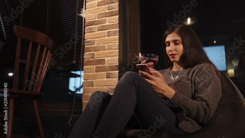 Stunning brunette woman is enjoying her evening in a cafe. She is drinking cocktail and using smartphone. photo