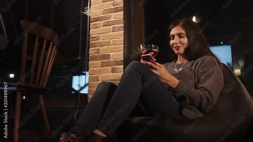 a young woman is in a chair in a bar, a lady holds an alcoholic cocktail and a mobile phone in her hand, she communicates with friends in social networks a young woman is in a chair in a bar, a lady holds an alcoholic cocktail and a mobile phone in her hand, she communicates with friends in social networks