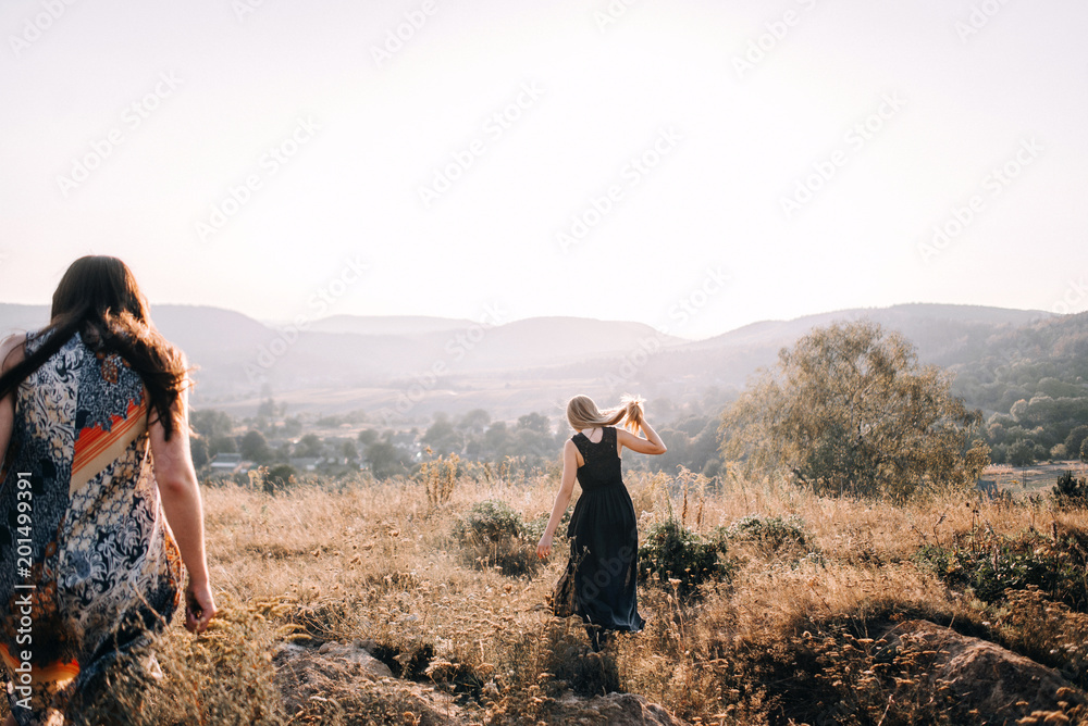 beautiful young girls walking in the light of long summer dresses for mountainous terrain, sand and posing. the wind and the sunset