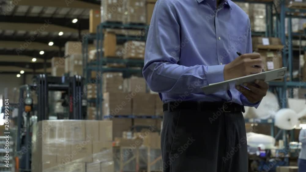 Man holding clip board and stocktaking, man pulling hand operated pallet truck in background of warehouse. Man holding clip board and stocktaking, man pulling hand operated pallet truck in background of warehouse.