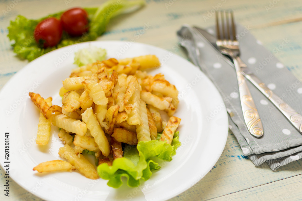 French fries with meat on a white plate on a wooden light background. French fries with meat on a white plate on a wooden light background.