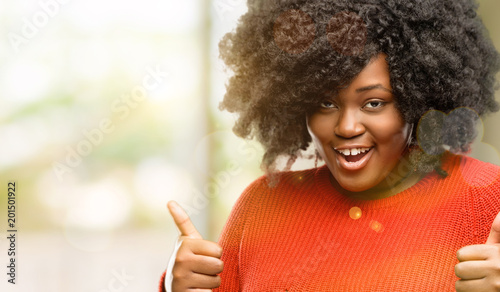 Beautiful african woman smiling broadly showing thumbs up gesture to camera, expression of like and approval, outdoor © Krakenimages.com