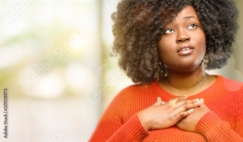 Картината върху платно Beautiful african woman having charming smile holding hands on heart wanting to