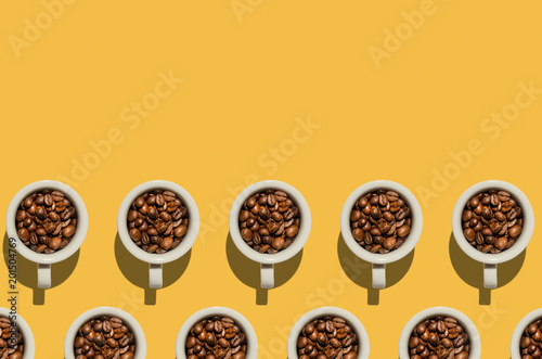 Cup concept. White cups with coffee beans on yellow background. Creative style.