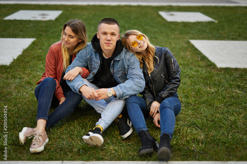 Boy with two girls on the green grass talking and smile to camera Boy with two girls on the green grass talking and smile to camera