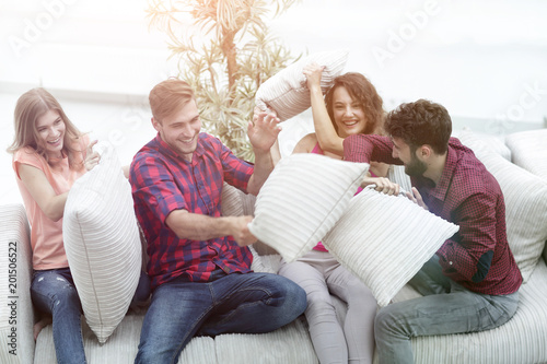 group of friends playing pillow fight, sitting on the couch