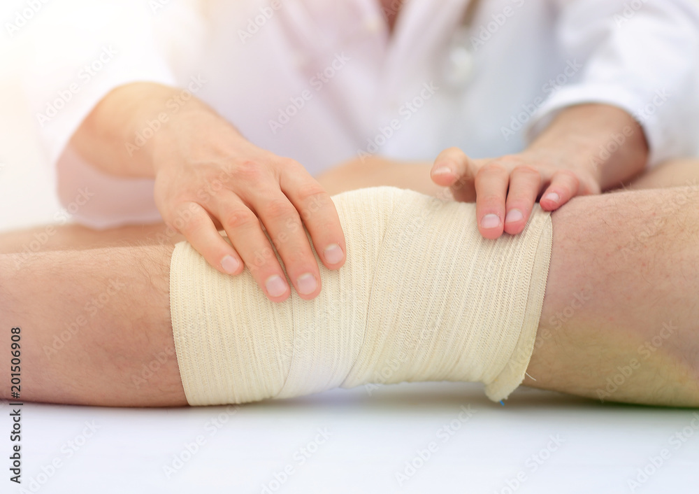 Mid section of doctor bandaging leg of patient in hospital Mid section of doctor bandaging leg of patient in hospital