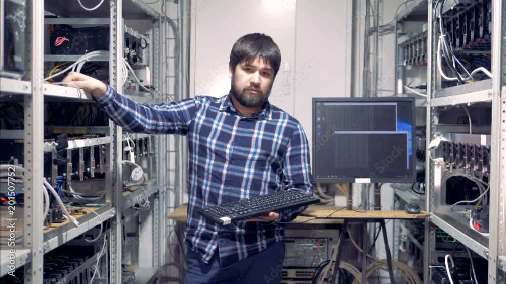 Cryptocurrency mining specialist is standing in a mining rig unit and looking into the camera