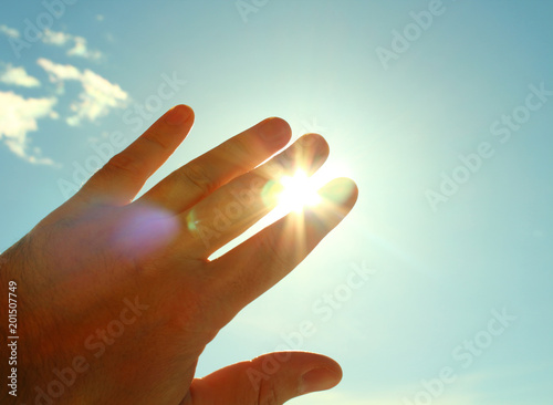The man's hand covers the sun. The man closes the palm of sunlight. Close-up. Background.