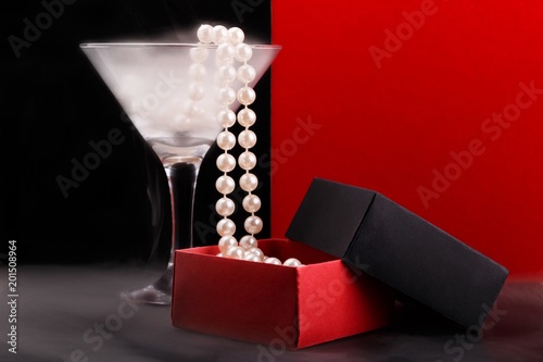 Wine glass with fog and perl beads falling into opened paper giftbox on foggy glossy surface