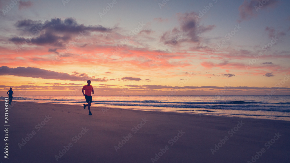 Two runners are running on the beach at sunrise.
