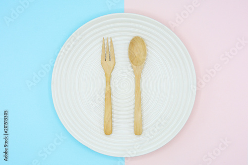 Spoons and forks in white ceramic dish on blue and pink background