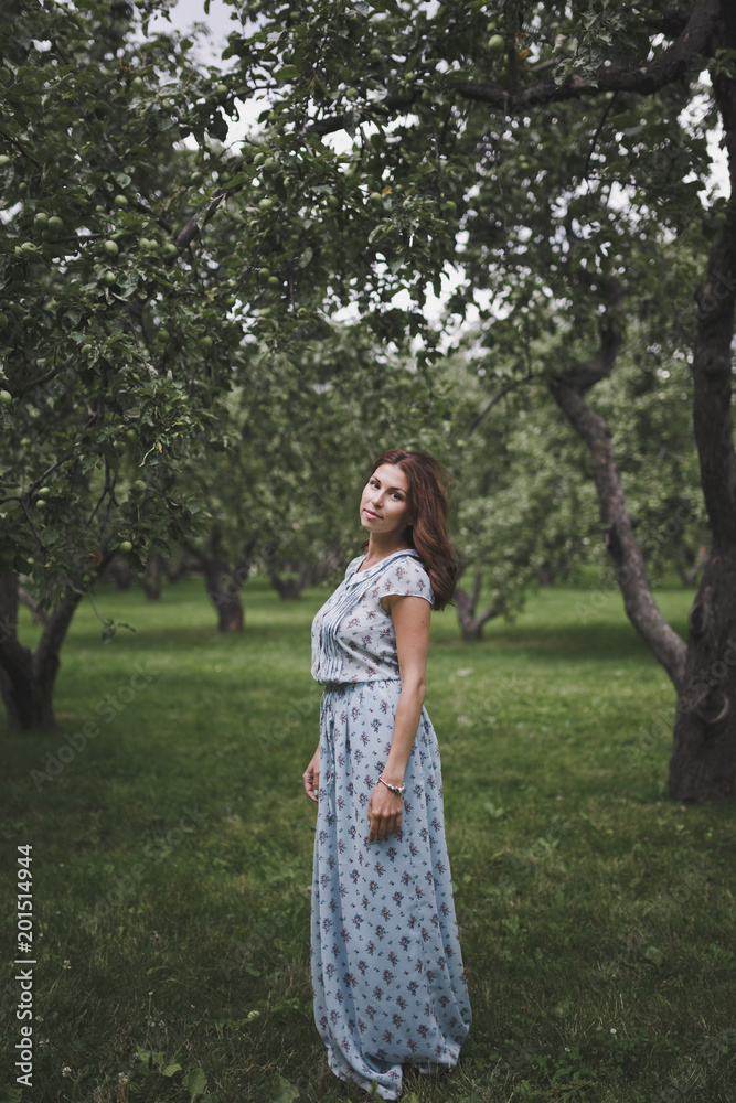 Beautiful smiling young brunette woman in a green summer garden amid the Apple trees with green fruit. Beautiful smiling young brunette woman in a green summer garden amid the Apple trees with green fruit.