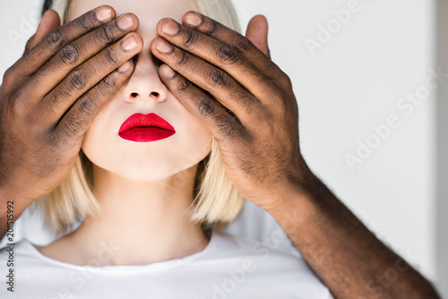 cropped image of african american boyfriend closing eyes of blonde girlfriend