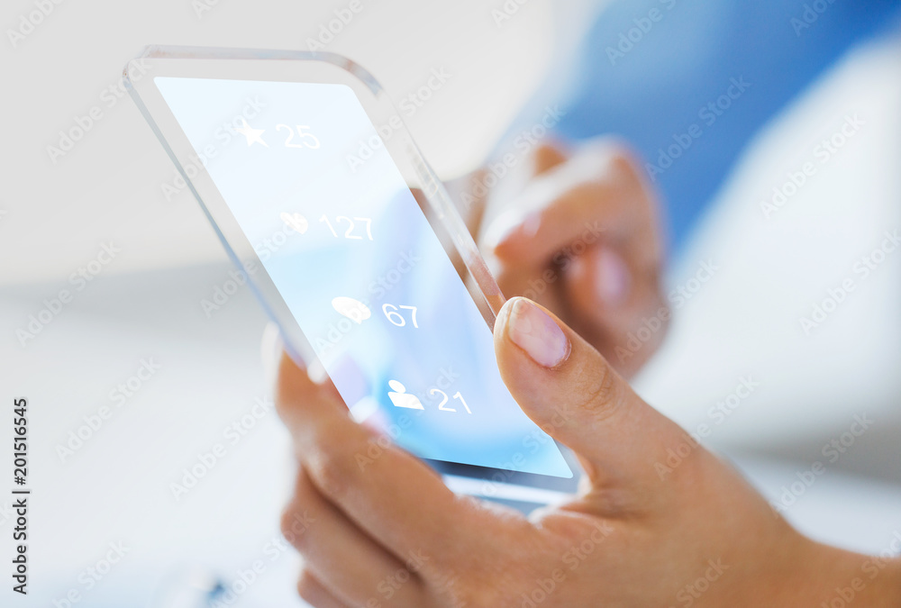 business, future technology and people concept - close up of female hand holding and showing transparent smartphone with social media icons over black background business, future technology and people concept - close up of female hand holding and showing transparent smartphone with social media icons over black background