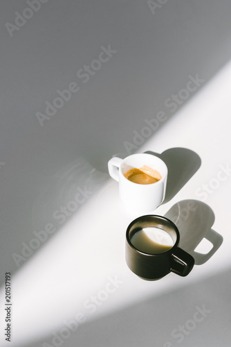 high angle view of black and white cups of milk and coffee on white surface