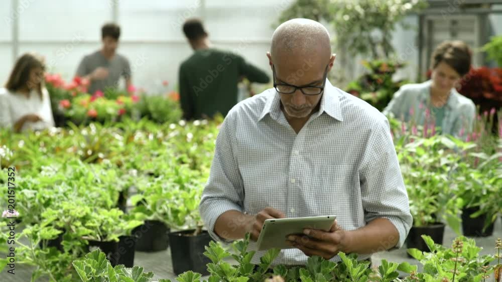 Man using digital tablet in garden centre, looking at camera, smiling. Man using digital tablet in garden centre, looking at camera, smiling.
