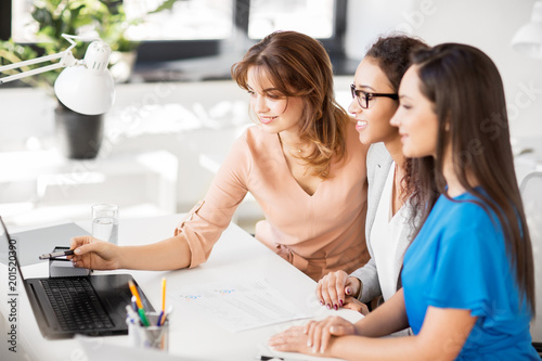 business, teamwork and people concept - female team or businesswomen with laptop computer working at office