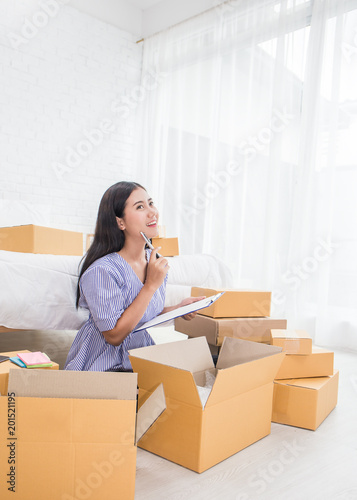 Startup small business entrepreneur SME, asian woman writing on clipboard. Portrait young small business owner at warehouse home office, online marketing packing delivery, SME e-commerce concept © paulaphoto