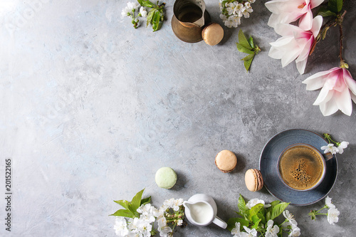 Blue cup of black espresso coffee french dessert macaroons, cream and spring flowers magnolia, blooming cherry branches over grey texture background. Top view, space. Spring greeting card, wallpapers