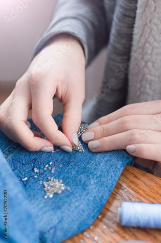 4127841 Beautiful female hands embroider with beads stars on denim.