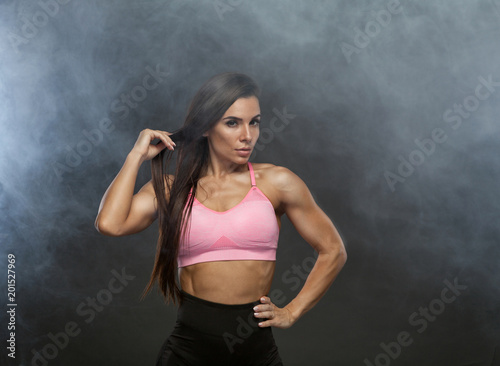 Image of fitness woman in sports clothing in the smoke. Young female model with muscular body. Horizontal studio shot with copy space on black background.