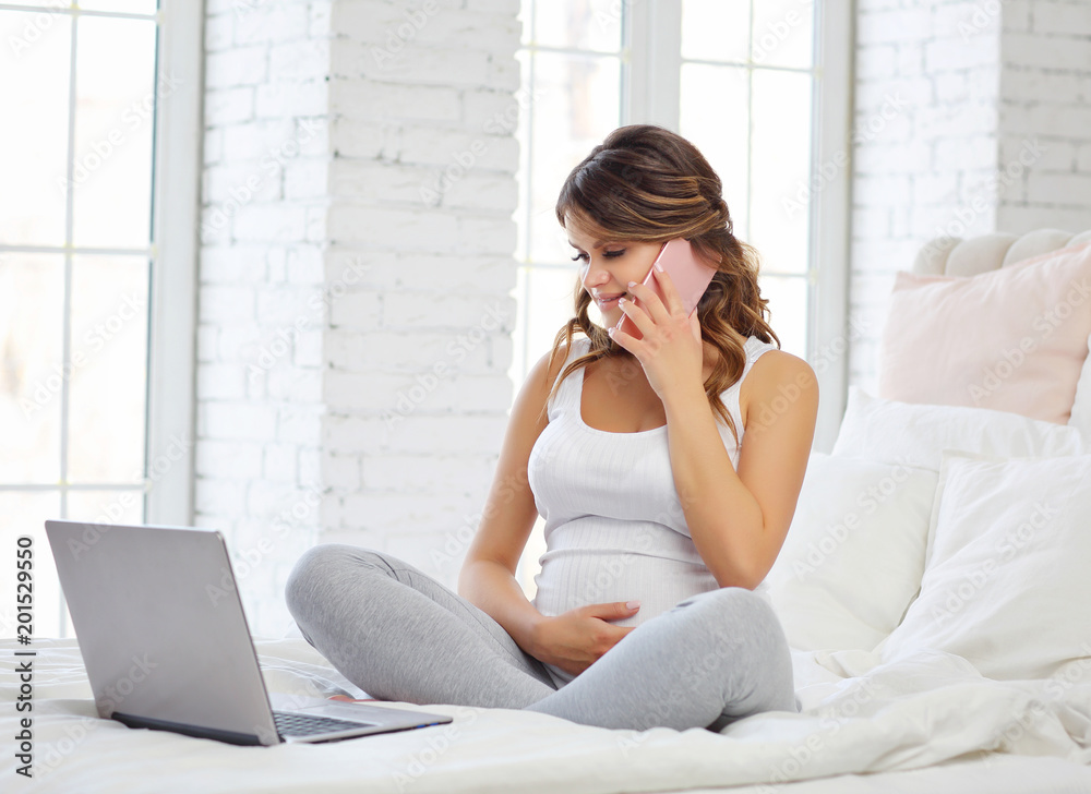 Portrait of a pregnant woman sitting on a bed with a computer. Concept of work during pregnancy. Portrait of a pregnant woman sitting on a bed with a computer. Concept of work during pregnancy.