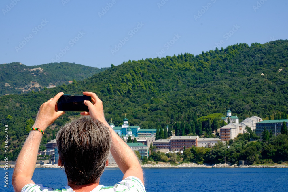 Man taking photo of greek monasteries on sea