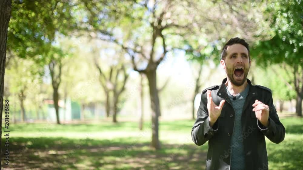 Hombre joven moreno con chaqueta verde bostezando en un parque/bosque Hombre joven moreno con chaqueta verde bostezando en un parque/bosque