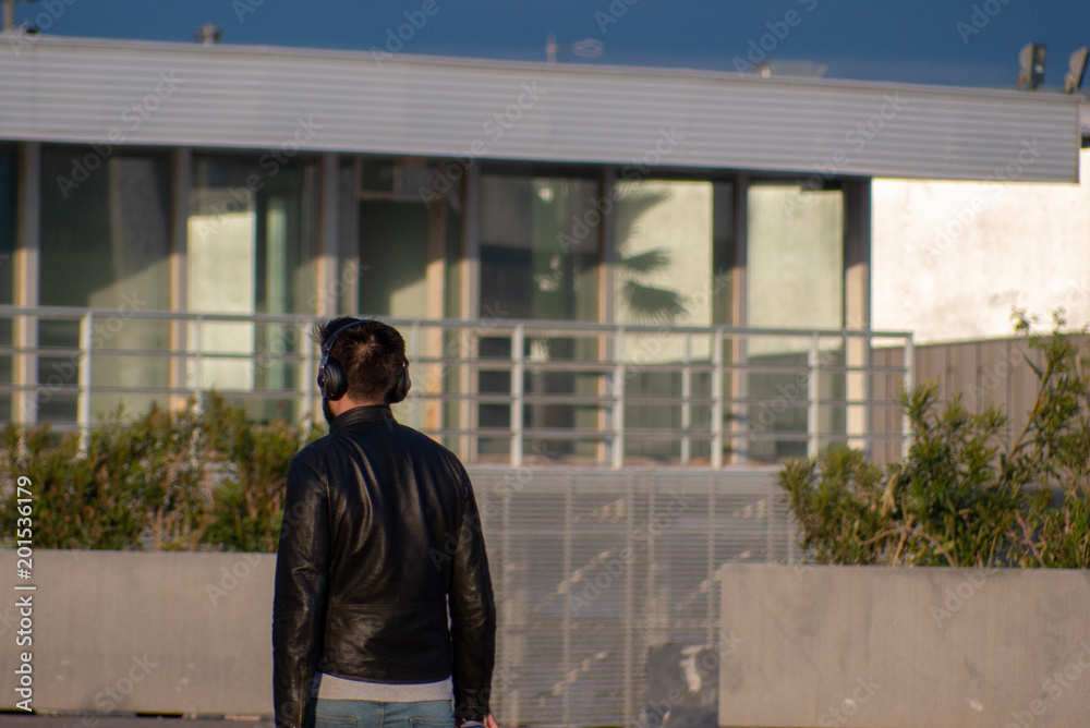 A guy in leather jacket or headphones with modern building background