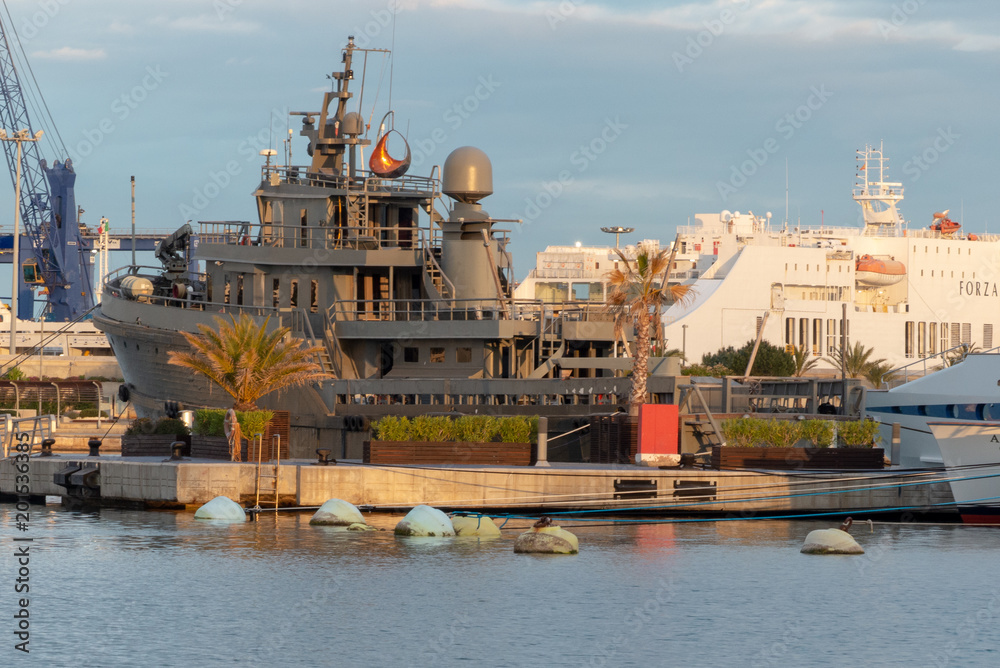 A gray classic boat moored in the port of Valencia with the ferry in the background with blue sky