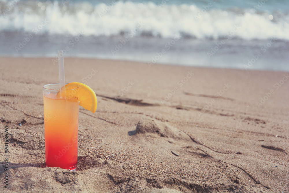 Glasses with colored cocktails on the beach with blue water in the background. Toned Glasses with colored cocktails on the beach with blue water in the background. Toned