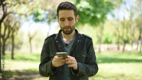 Hombre joven moreno con chaqueta verde mirando el móvil en un parque/bosque
