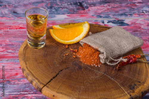 Mezcal - traditional Mexican strong alcoholic drink with orange slices, worm salt and chili papper on a old wooden board. photo