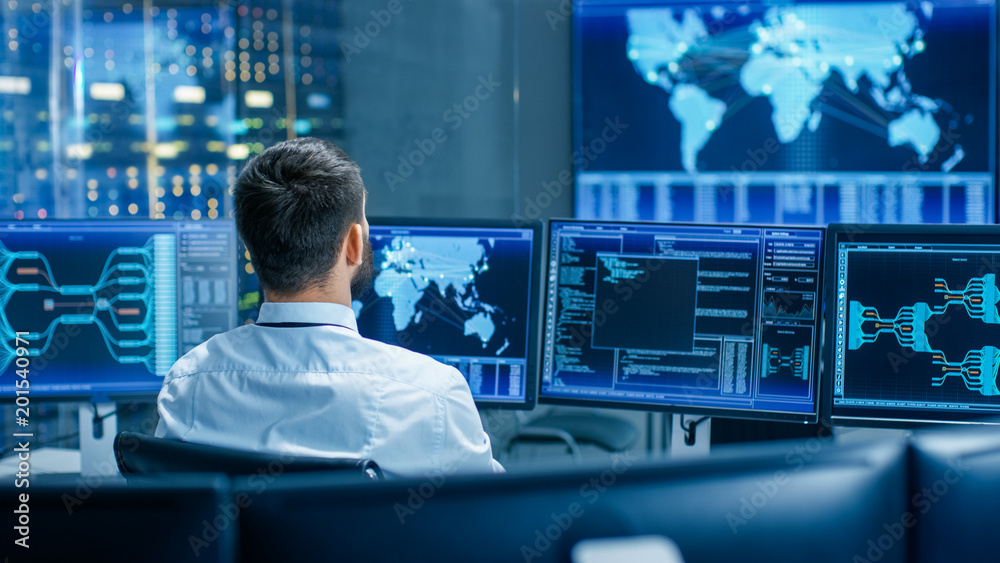 Back View in the System Control Center Operator Working. Multiple Screens Showing Technical Data. Back View in the System Control Center Operator Working. Multiple Screens Showing Technical Data.