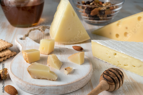 Different kinds of cheeses on white wooden board with nuts, honey and herbs.