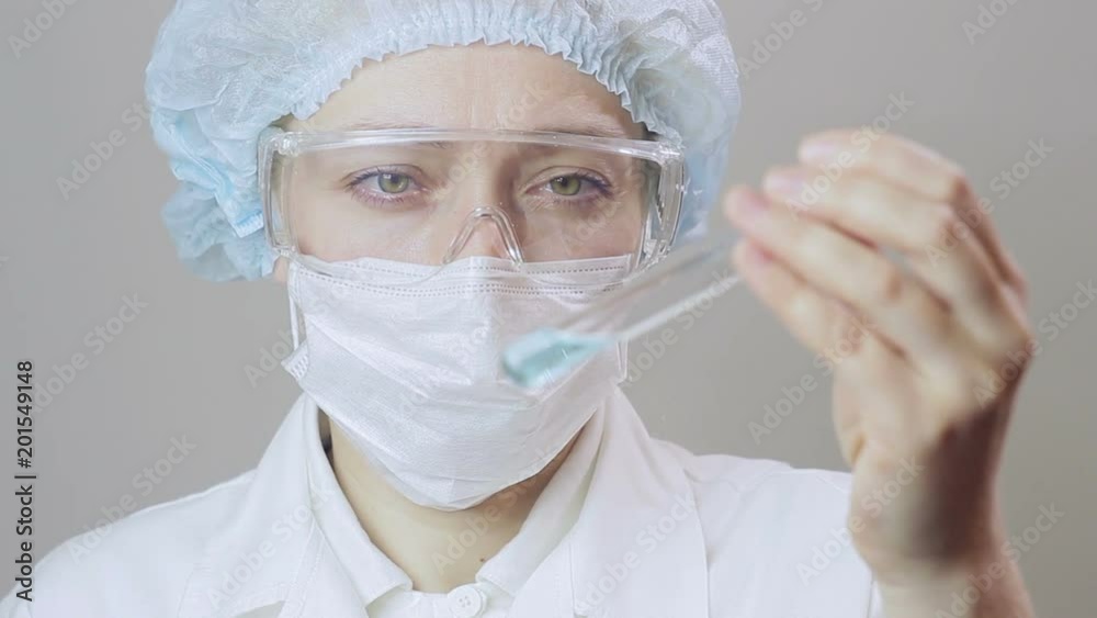 Closeup of a female doctor in white clothes and protective gloves pouring a blue liquid into a test tube Closeup of a female doctor in white clothes and protective gloves pouring a blue liquid into a test tube