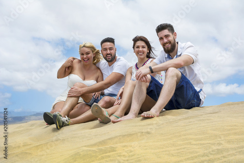 Four friends sitting on the sand dunes.