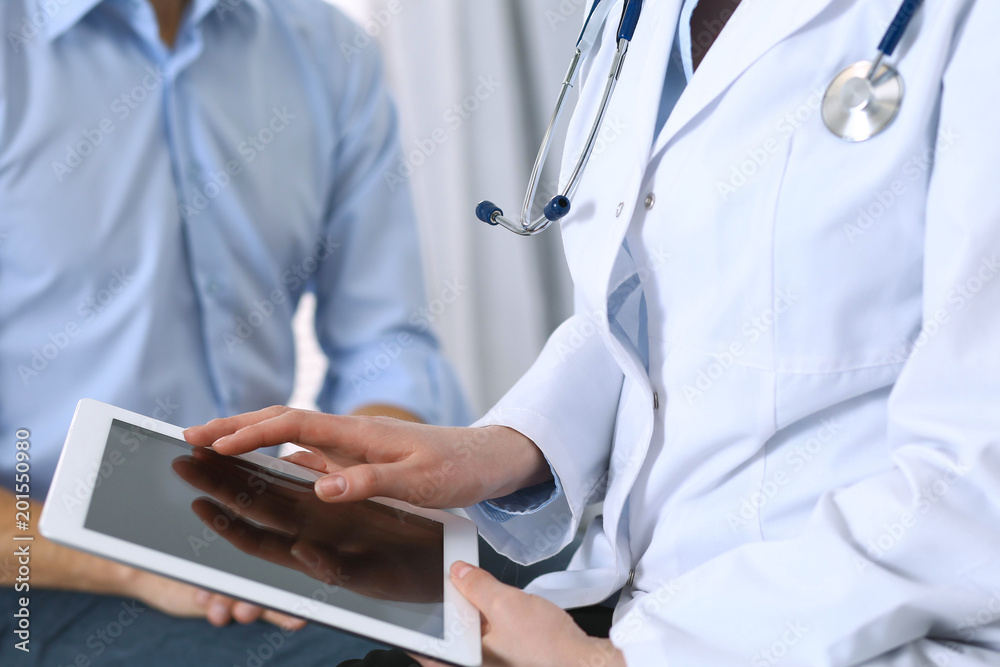 Female doctor using touchpad or tablet computer while consulting man patient in hospital. Medicine and healthcare concept Female doctor using touchpad or tablet computer while consulting man patient in hospital. Medicine and healthcare concept