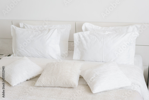 Fototapeta Naklejka Na Ścianę i Meble -  Comfortable soft pillows on the bed. Close-up white bedding sheets and pillow on light wall room background. Fresh bed concept