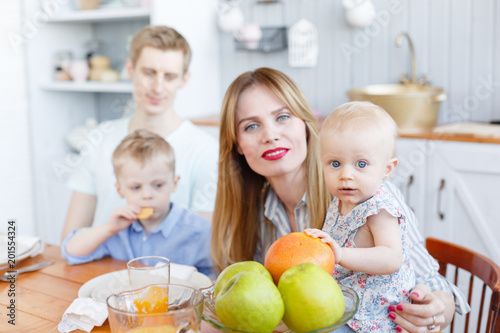 So cute family. Young mother and father with her baby daughter and son. Modern kitchen setting. Funny girl with mom on kitchen.