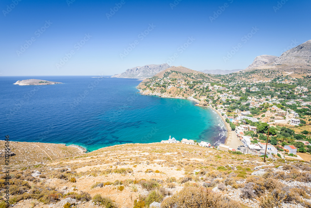 Beautiful sunny coast view to the greek blue sea with crystal clear water beach with some boats fishing cruising surrounded by hills mountains, Kantouni, Patmos, Kos, Dodecanese Islands, Greece 
